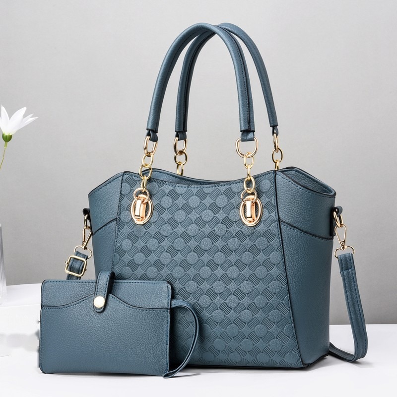 Blaue Schultertasche mit Prägemuster und kleinem blauem Täschchen, im Hintergrund eine weiße Blume