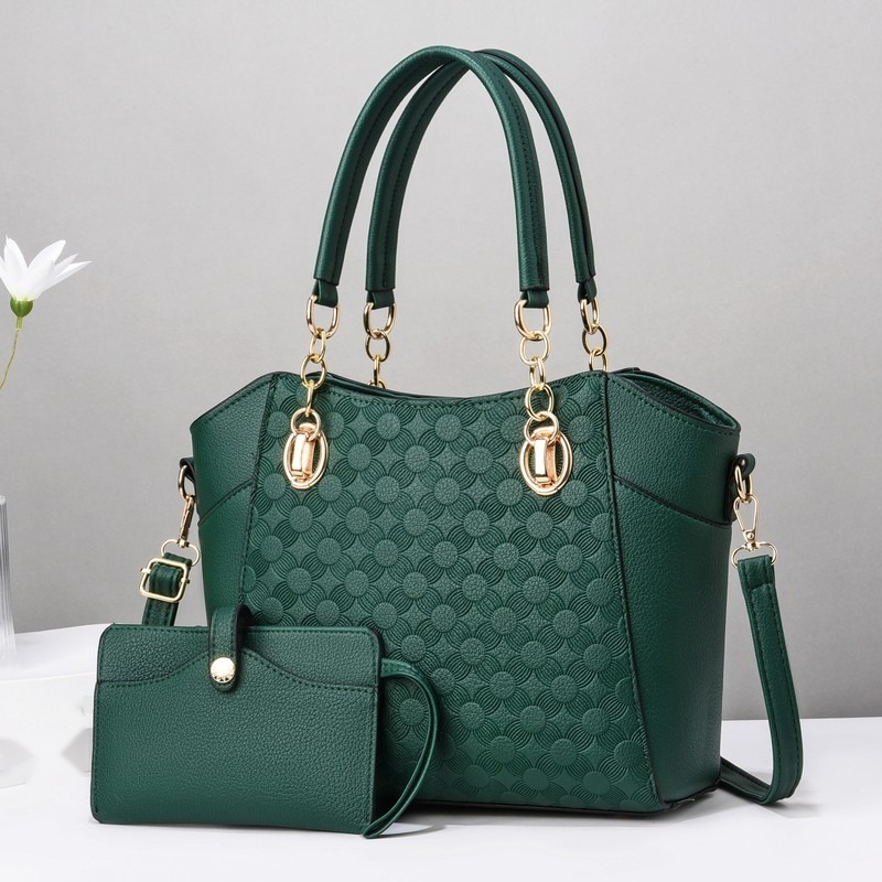 Dunkelgrüne Schultertasche mit Prägemuster und kleinem grünem Täschchen vor grauem Hintergrund