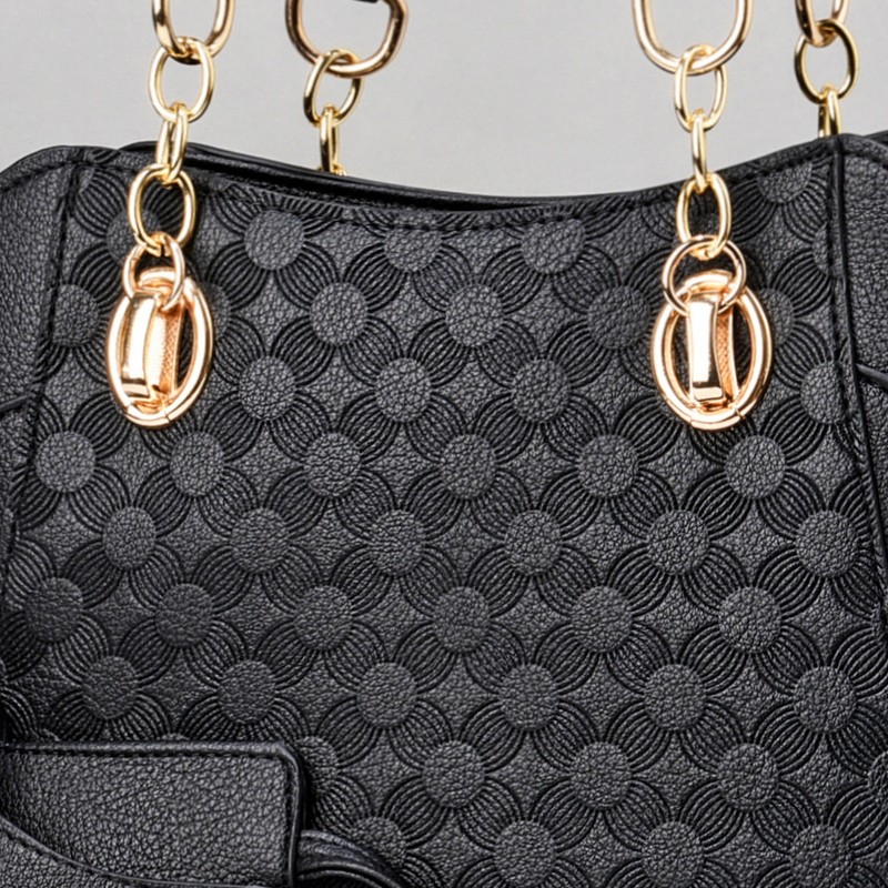 Nahaufnahme des Prägemusters der schwarzen Tasche mit Metallbeschlägen in Goldfarbe